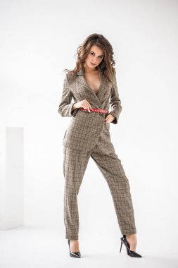 Kırmızı kemer, beyaz duvar arka plan üzerinde duran ile rahat takım elbise giyen güzel kıvırcık kadın moda stüdyo portre kareli 