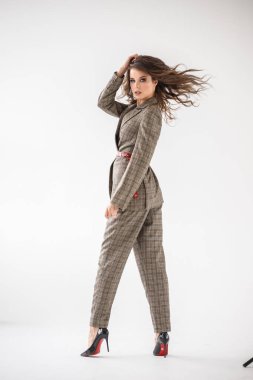 Kırmızı kemer, beyaz duvar arka plan üzerinde duran ile rahat takım elbise giyen güzel kıvırcık kadın moda stüdyo portre kareli 