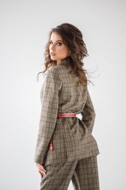 Kırmızı kemer, beyaz duvar arka plan üzerinde duran ile rahat takım elbise giyen güzel kıvırcık kadın moda stüdyo portre kareli 