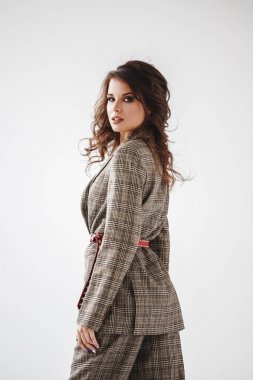 Kırmızı kemer, beyaz duvar arka plan üzerinde duran ile rahat takım elbise giyen güzel kıvırcık kadın moda stüdyo portre kareli 