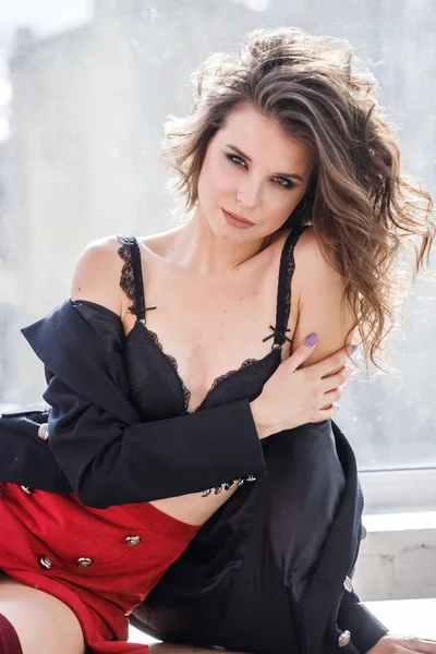 Gün ışığında ahşap pencere yatan kırmızı etek, siyah ceket ve siyah iç çamaşırı giyen güzel kıvırcık kadın moda studio portresi