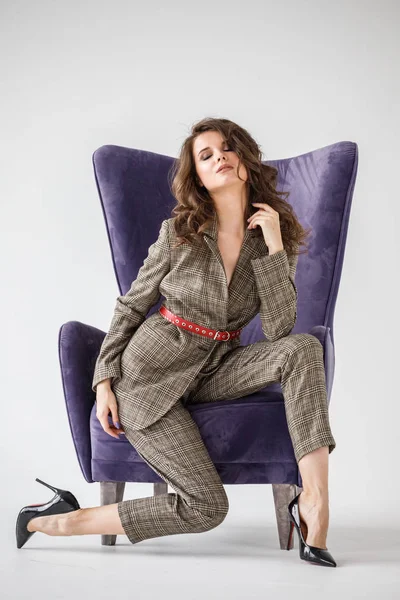 Kırmızı kemer, mor koltuk, beyaz duvar arka plan oturan sıradan takım elbise giyen güzel kıvırcık kadın moda stüdyo portre kareli 
