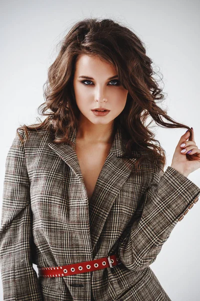 Kırmızı kemer, beyaz duvar arka plan üzerinde duran ile rahat takım elbise giyen güzel kıvırcık kadın moda stüdyo portre kareli 