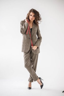 Damalı rahat takım ve siyah sütyen, ellerinde kırmızı kemer ile gri duvar arka plan üzerinde duran güzel kıvırcık kadın moda studio portresi