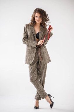 Damalı rahat takım ve siyah sütyen, ellerinde kırmızı kemer ile gri duvar arka plan üzerinde duran güzel kıvırcık kadın moda studio portresi