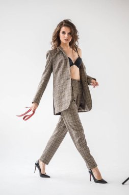 Damalı rahat takım ve siyah sütyen, ellerinde kırmızı kemer ile gri duvar arka plan üzerinde duran güzel kıvırcık kadın moda studio portresi