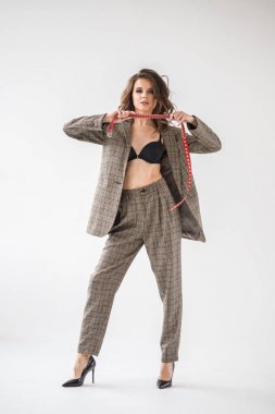 Damalı rahat takım ve siyah sütyen, ellerinde kırmızı kemer ile gri duvar arka plan üzerinde duran güzel kıvırcık kadın moda studio portresi