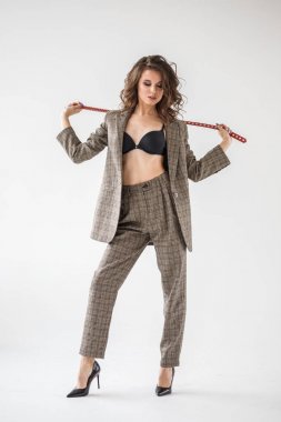 Damalı rahat takım ve siyah sütyen, ellerinde kırmızı kemer ile gri duvar arka plan üzerinde duran güzel kıvırcık kadın moda studio portresi