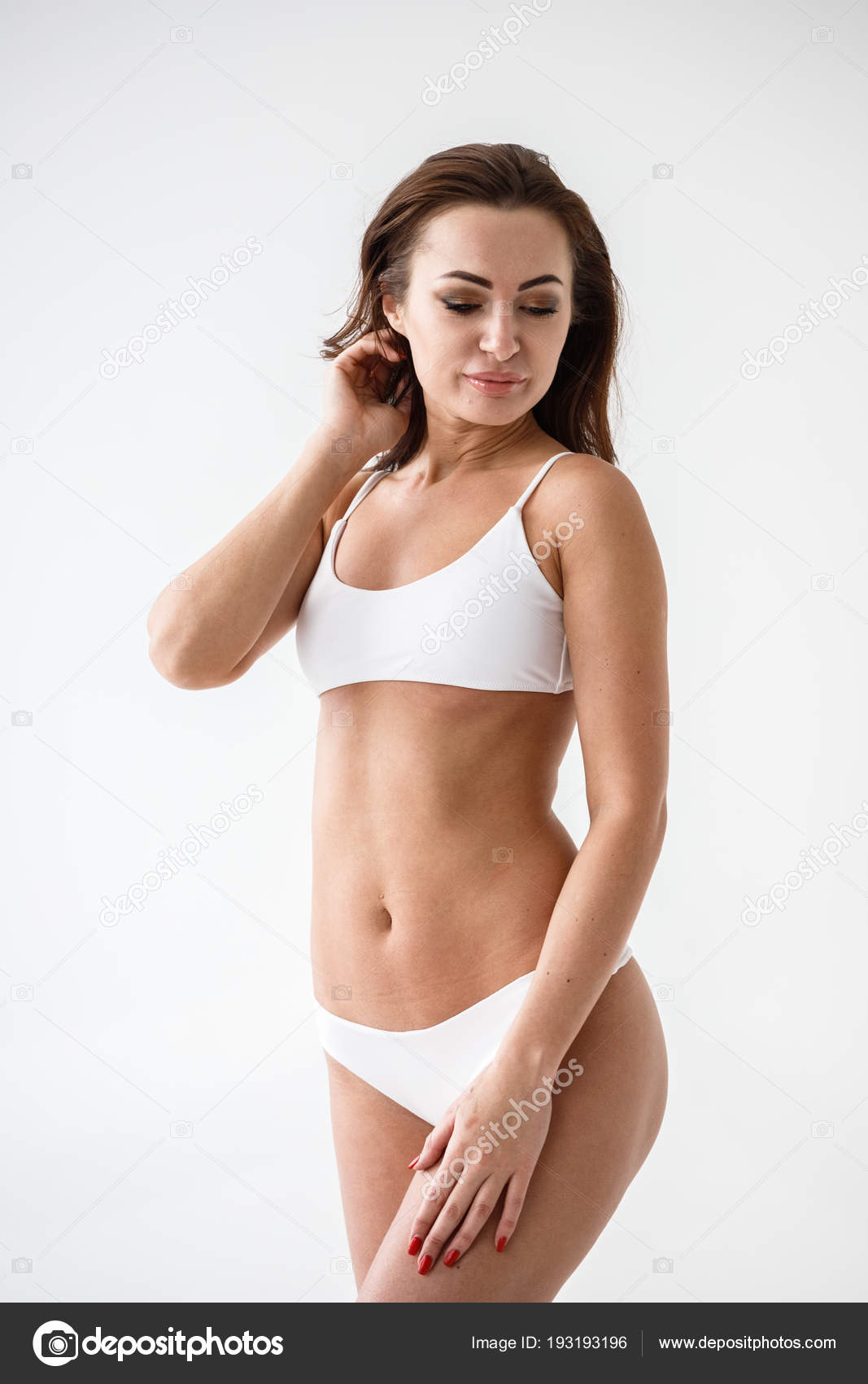 Portrait of sexy beautiful brunette girl posing in white underclothes.  Studio. White wall. Isolated. Tattoo on the hip Stock Photo