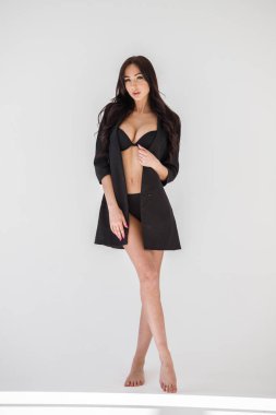 Seksi siyah iç çamaşırı ve siyah ceket ayakta beyaz duvar arka plan üzerinde giyen genç esmer kız portresi stüdyo