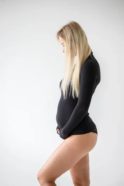 スタジオポートレートの妊娠中のブロンド女性で黒服に立って白い壁の背景 — ストック写真