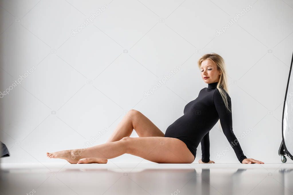 Studio portrait of sporty blond woman in black clothes sitting on floor, white wall background