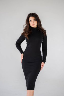 Gri duvar arkasında poz veren siyah elbiseli güzel esmer kadının şık stüdyo portresi.  