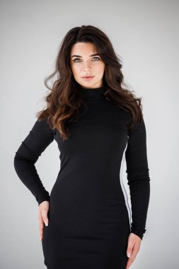 Gri duvar arkasında poz veren siyah elbiseli güzel esmer kadının şık stüdyo portresi.  