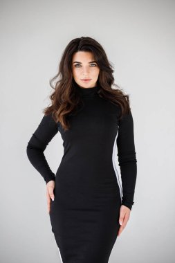 Gri duvar arkasında poz veren siyah elbiseli güzel esmer kadının şık stüdyo portresi.  