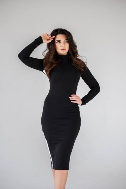 Gri duvar arkasında poz veren siyah elbiseli güzel esmer kadının şık stüdyo portresi.  