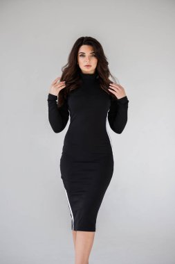 Gri duvar arkasında poz veren siyah elbiseli güzel esmer kadının şık stüdyo portresi.  