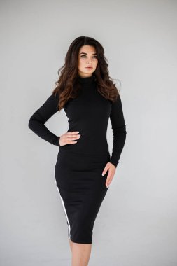 Gri duvar arkasında poz veren siyah elbiseli güzel esmer kadının şık stüdyo portresi.  