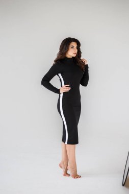 Gri duvar arkasında poz veren siyah elbiseli güzel esmer kadının şık stüdyo portresi.  