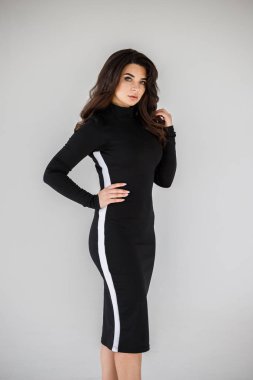 Gri duvar arkasında poz veren siyah elbiseli güzel esmer kadının şık stüdyo portresi.  