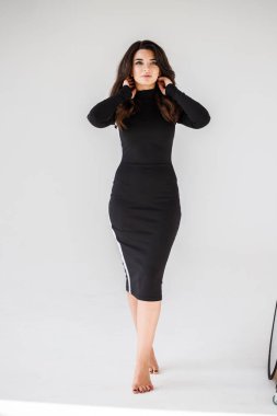 Gri duvar arkasında poz veren siyah elbiseli güzel esmer kadının şık stüdyo portresi.  