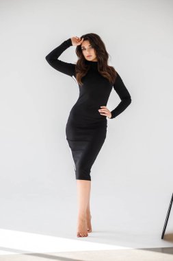 Gri duvar arkasında poz veren siyah elbiseli güzel esmer kadının şık stüdyo portresi.  