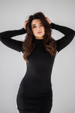 Gri duvar arkasında poz veren siyah elbiseli güzel esmer kadının şık stüdyo portresi.  