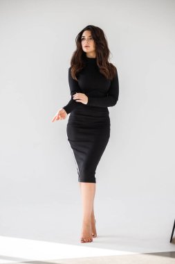 Gri duvar arkasında poz veren siyah elbiseli güzel esmer kadının şık stüdyo portresi.  