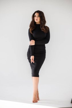 Gri duvar arkasında poz veren siyah elbiseli güzel esmer kadının şık stüdyo portresi.  