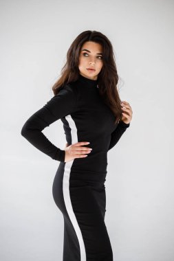 Gri duvar arkasında poz veren siyah elbiseli güzel esmer kadının şık stüdyo portresi.  