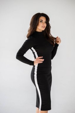 Gri duvar arkasında poz veren siyah elbiseli güzel esmer kadının şık stüdyo portresi.  