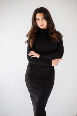 Gri duvar arkasında poz veren siyah elbiseli güzel esmer kadının şık stüdyo portresi.  