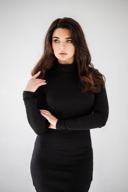 Gri duvar arkasında poz veren siyah elbiseli güzel esmer kadının şık stüdyo portresi.  