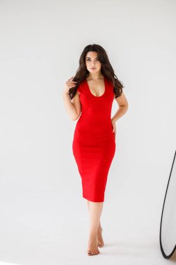 Gri duvar arkasında poz veren kırmızı elbiseli güzel esmer kadının şık stüdyo portresi.  