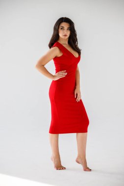 Gri duvar arkasında poz veren kırmızı elbiseli güzel esmer kadının şık stüdyo portresi.  