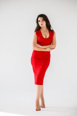 Gri duvar arkasında poz veren kırmızı elbiseli güzel esmer kadının şık stüdyo portresi.  