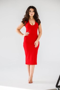 Gri duvar arkasında poz veren kırmızı elbiseli güzel esmer kadının şık stüdyo portresi.  