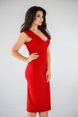 Gri duvar arkasında poz veren kırmızı elbiseli güzel esmer kadının şık stüdyo portresi.  