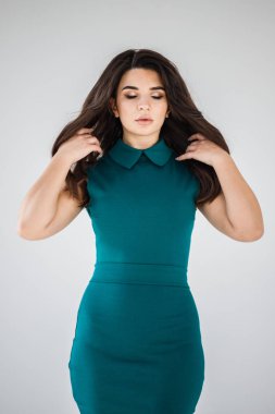 Cyan elbiseli esmer kadının gri duvar arkasında poz veren şık stüdyo portresi.  