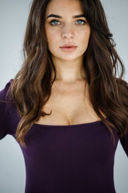 Mor elbiseli, gri duvar arkasında poz veren güzel esmer kadının şık stüdyo portresi.  