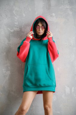 Güzel kız kapüşonlu seksi esmer duvarın yanında poz veriyor.