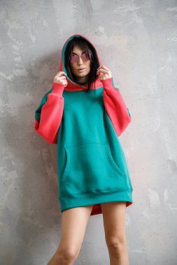 Güzel kız kapüşonlu seksi esmer duvarın yanında poz veriyor.