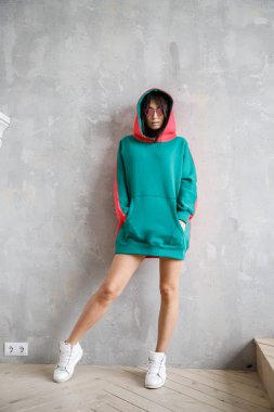 Güzel kız kapüşonlu seksi esmer duvarın yanında poz veriyor.