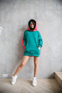 Güzel kız kapüşonlu seksi esmer duvarın yanında poz veriyor.