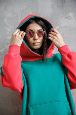 Güzel kız kapüşonlu seksi esmer duvarın yanında poz veriyor.