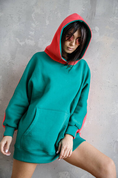 Beautiful girl sexy brunette in a hoodie posing near the wall