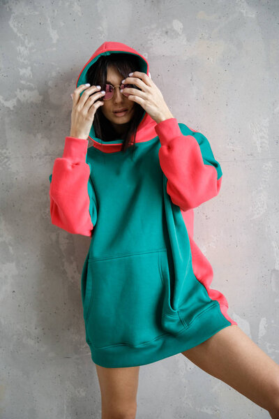 Beautiful girl sexy brunette in a hoodie posing near the wall