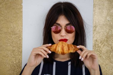 Gözlüklü güzel esmer kız apartmanın içinde kruvasan yiyor. 