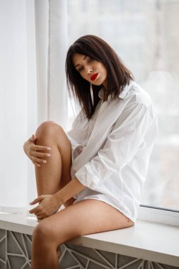 Beyaz gömlekli çekici esmer, sabah pencerenin yanında poz veriyor. 