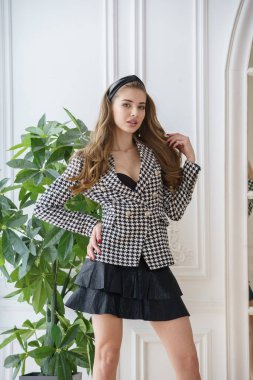 Gayri resmi takım elbiseli güzel bir manken ve yüksek topuklu ayakkabılar tencerede yeşil bir fabrikanın yanında duruyor. 